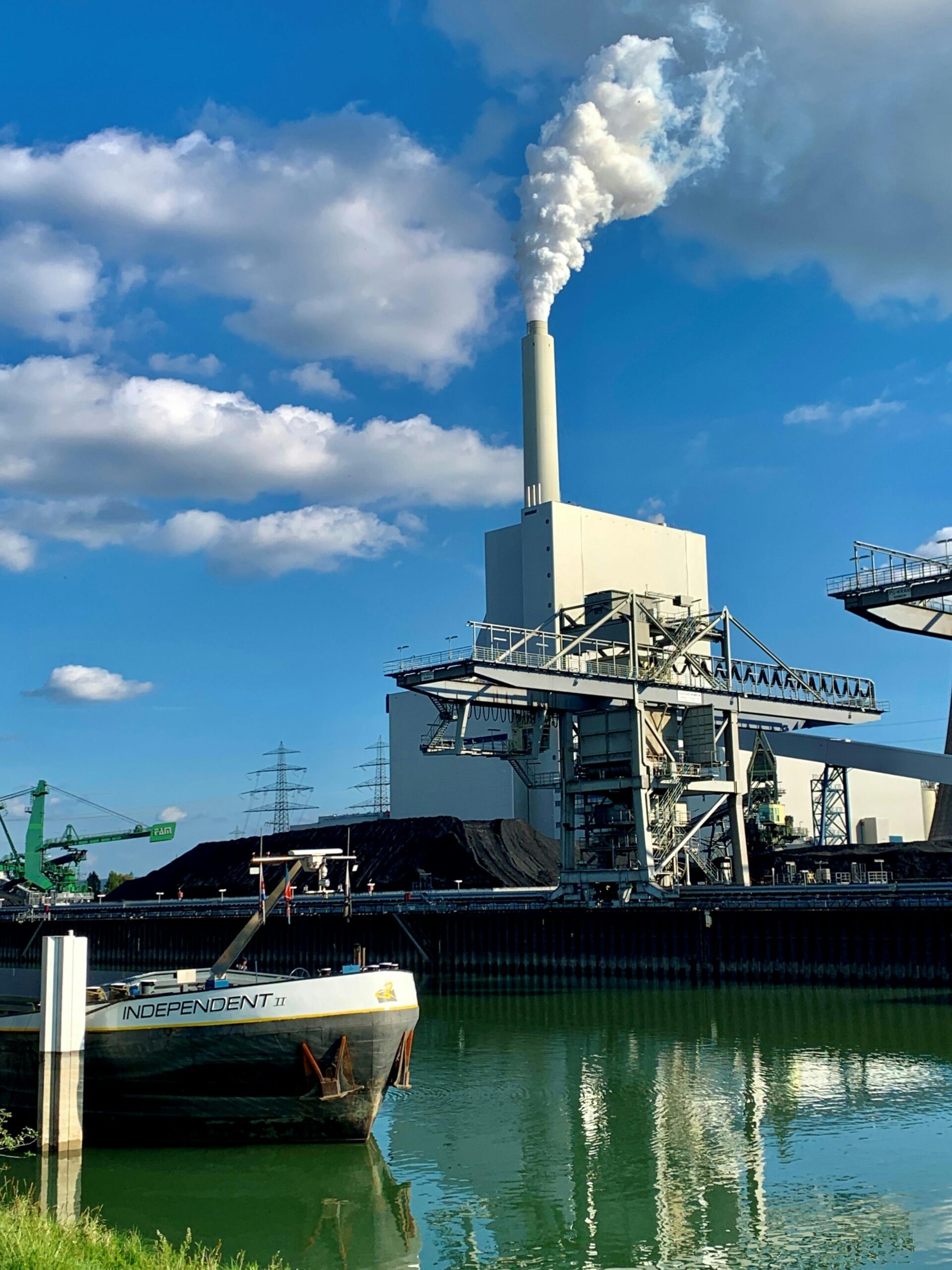 Smoke rises from a power plant smokestack near water with a boat in Karlsruhe, Germany.
