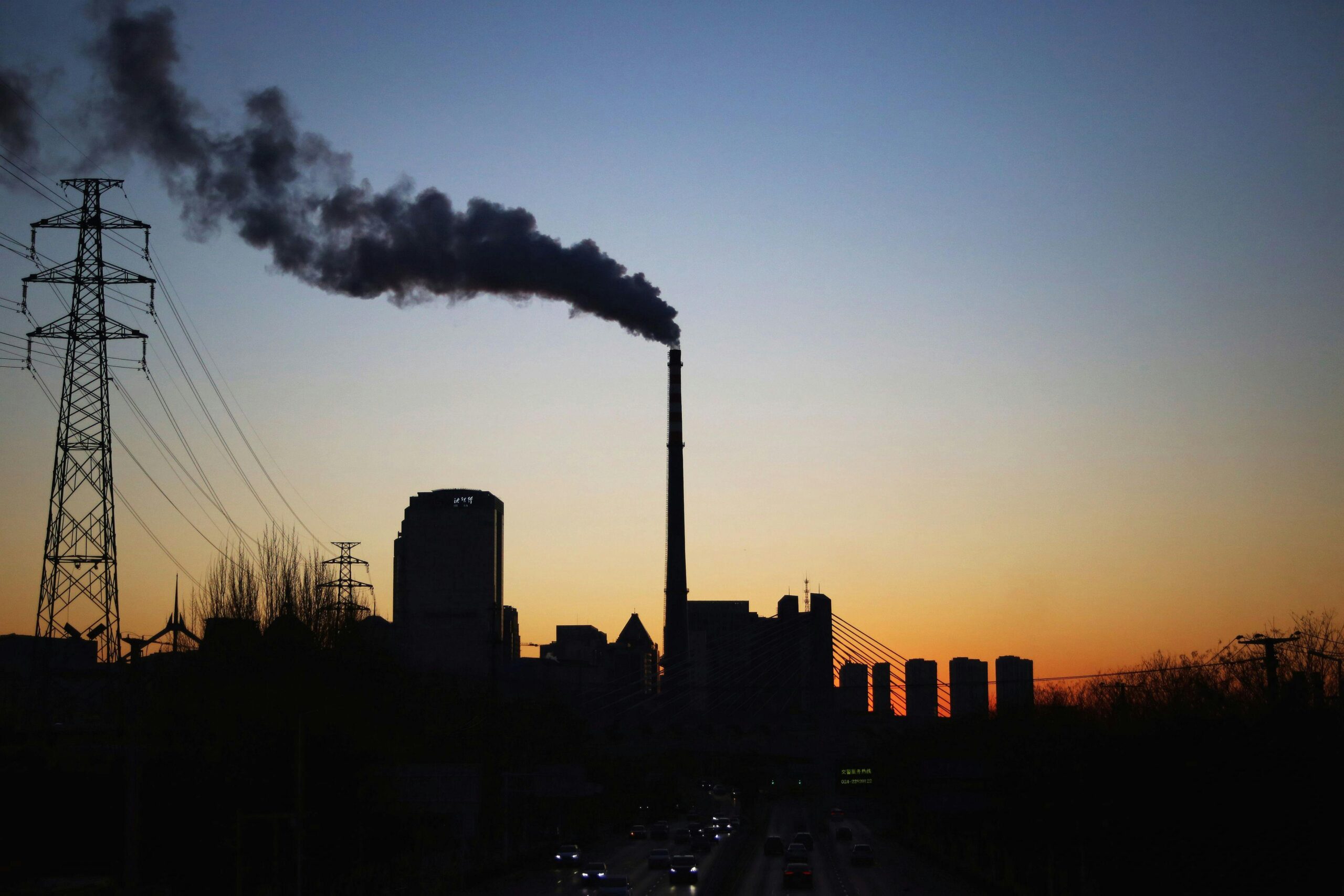 Dramatic sunset silhouette of an industrial smokestack with pollution in the urban skyline.